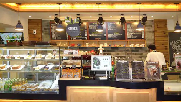 Un comptoir de boulangerie où sont exposés divers produits de boulangerie et pâtisseries, ainsi qu’un tableau affichant le menu et une personne derrière le comptoir.