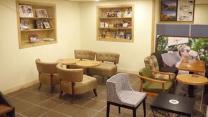 Un espace salon confortable, aménagé avec des canapés et des fauteuils, une petite table et des étagères murales où sont disposés des livres et des magazines.