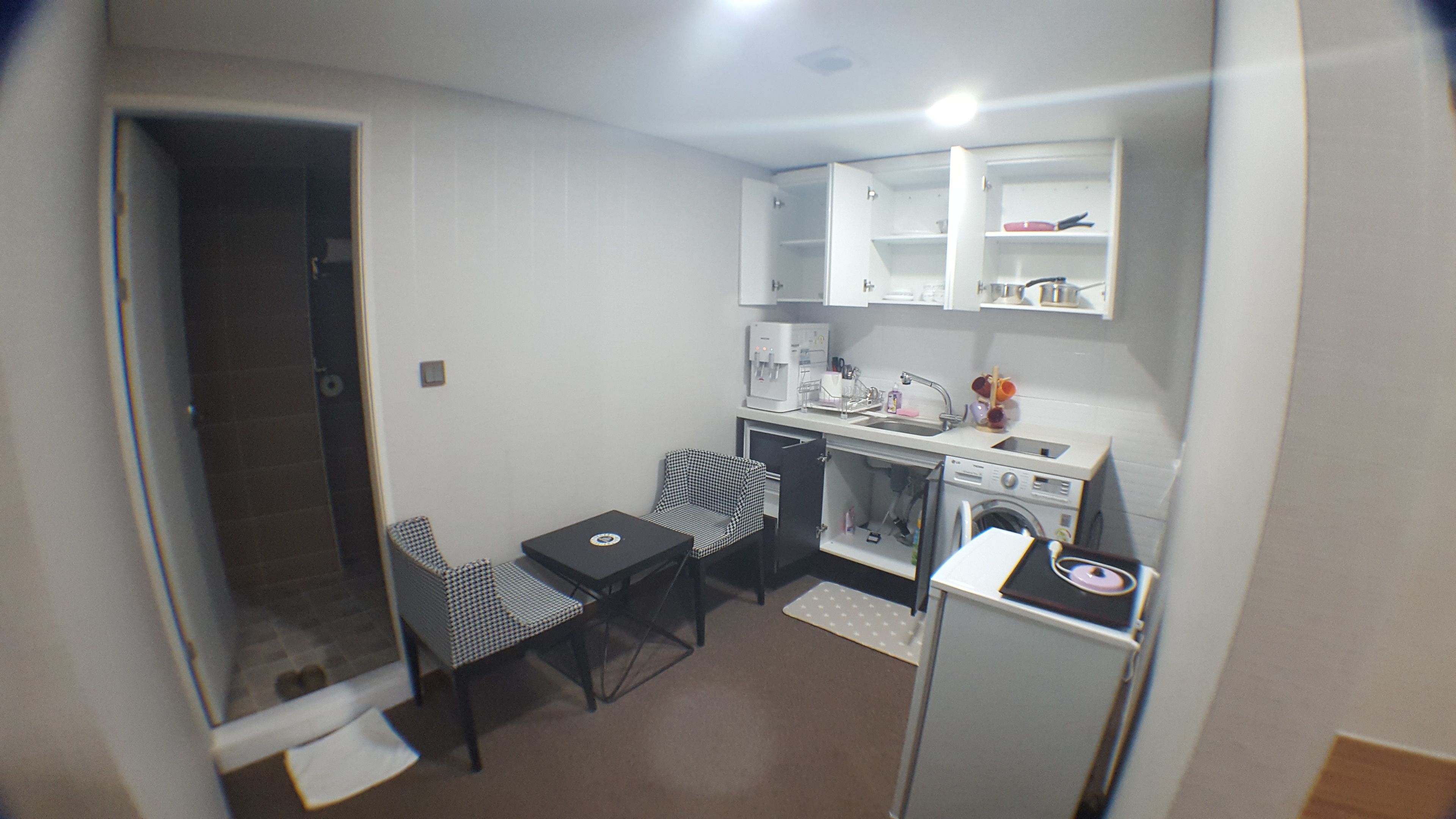A compact kitchenette with a microwave, sink, and small refrigerator. There is a chair and a table with a placemat.
