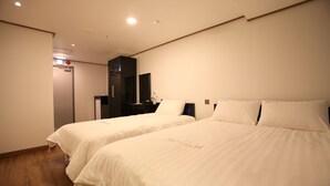 Une chambre d’hôtel avec deux lits simples, un petit bureau, un miroir et une porte.