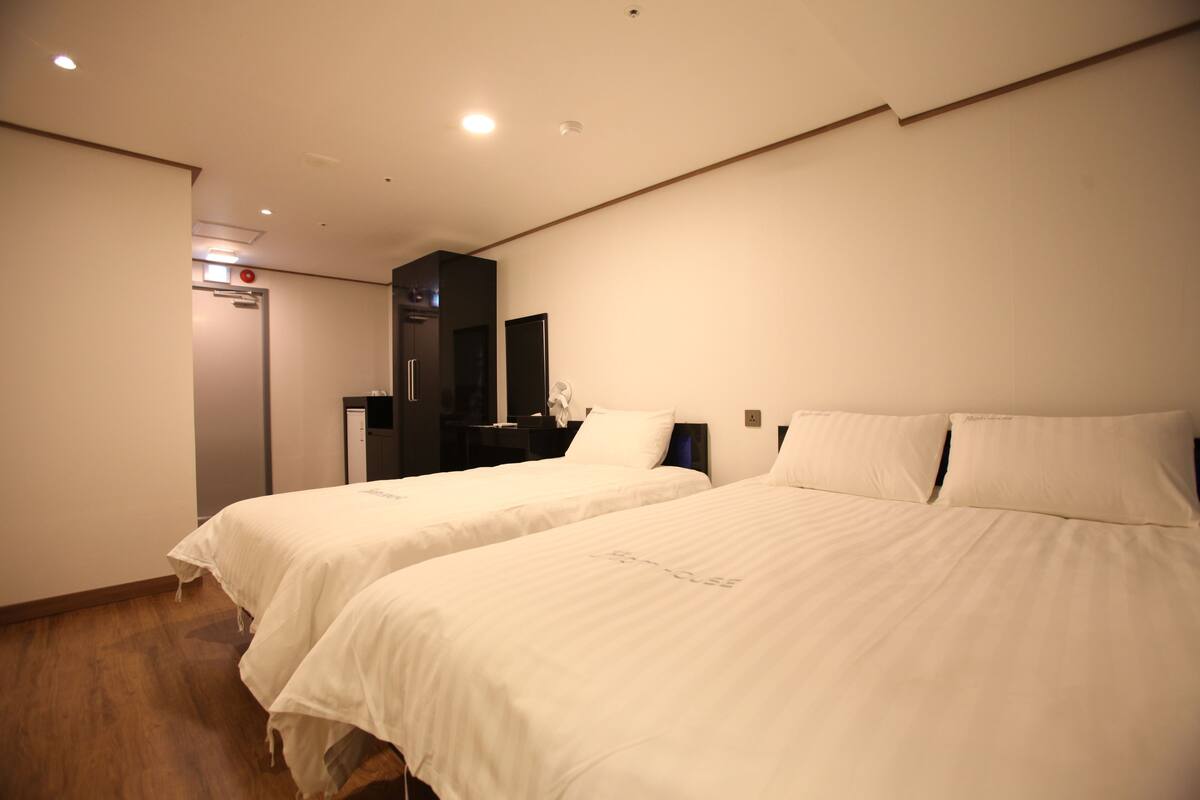 Habitación de hotel con dos camas individuales, un escritorio pequeño, un espejo y una puerta.
