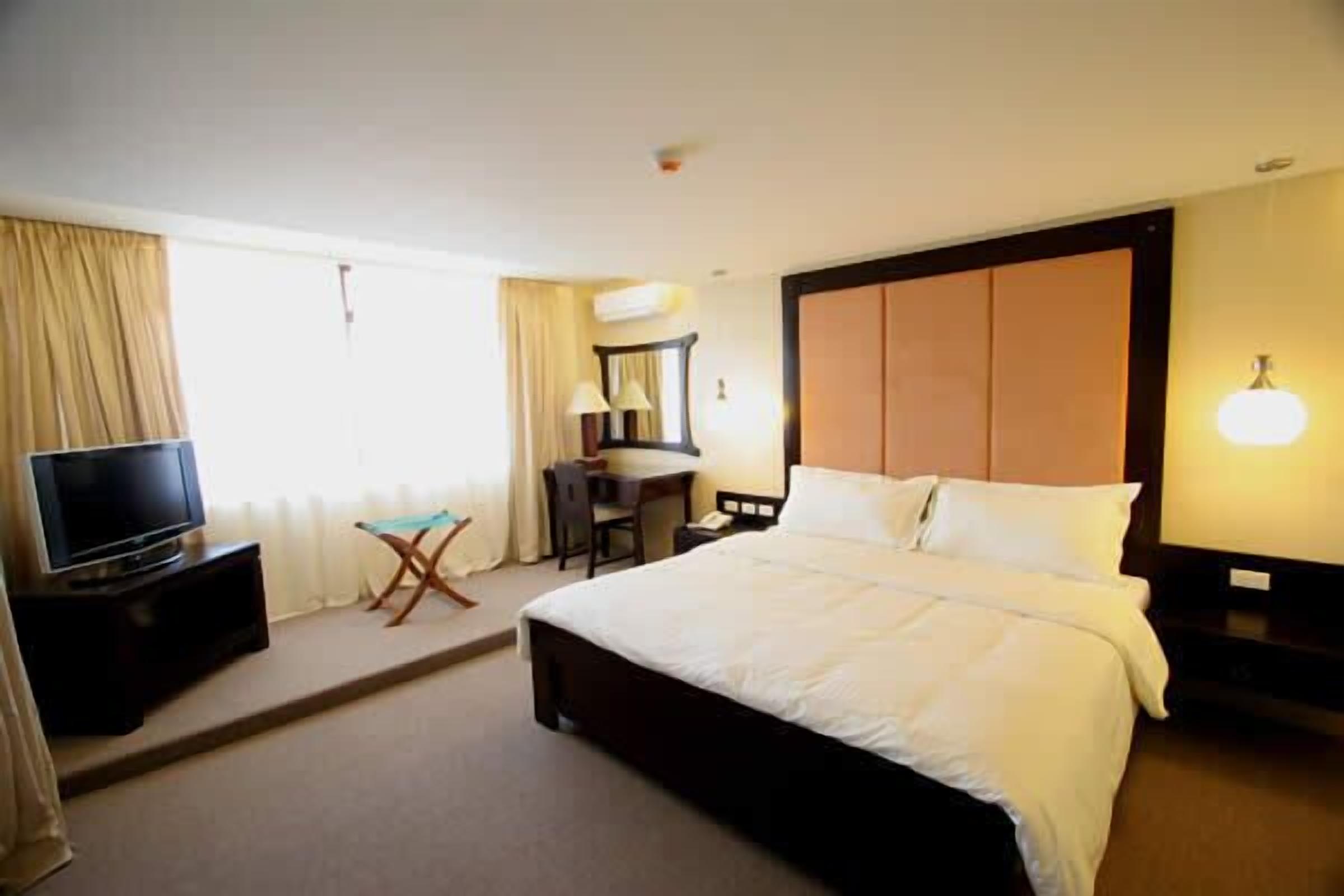 A hotel room with a large bed, a desk with a chair, a television, and a lamp.