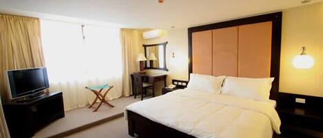A hotel room with a large bed, a desk with a chair, a television, and a lamp.