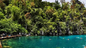 Una playa tropical con agua turquesa cristalina, rodeada de abundante follaje verde y afloramientos rocosos.