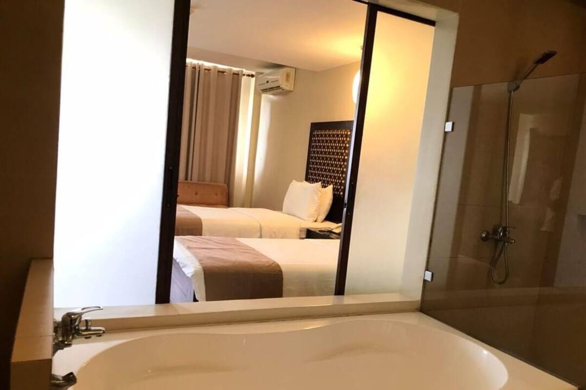 Un baño de hotel con una bañera grande, ducha y una cama visible en el espejo.