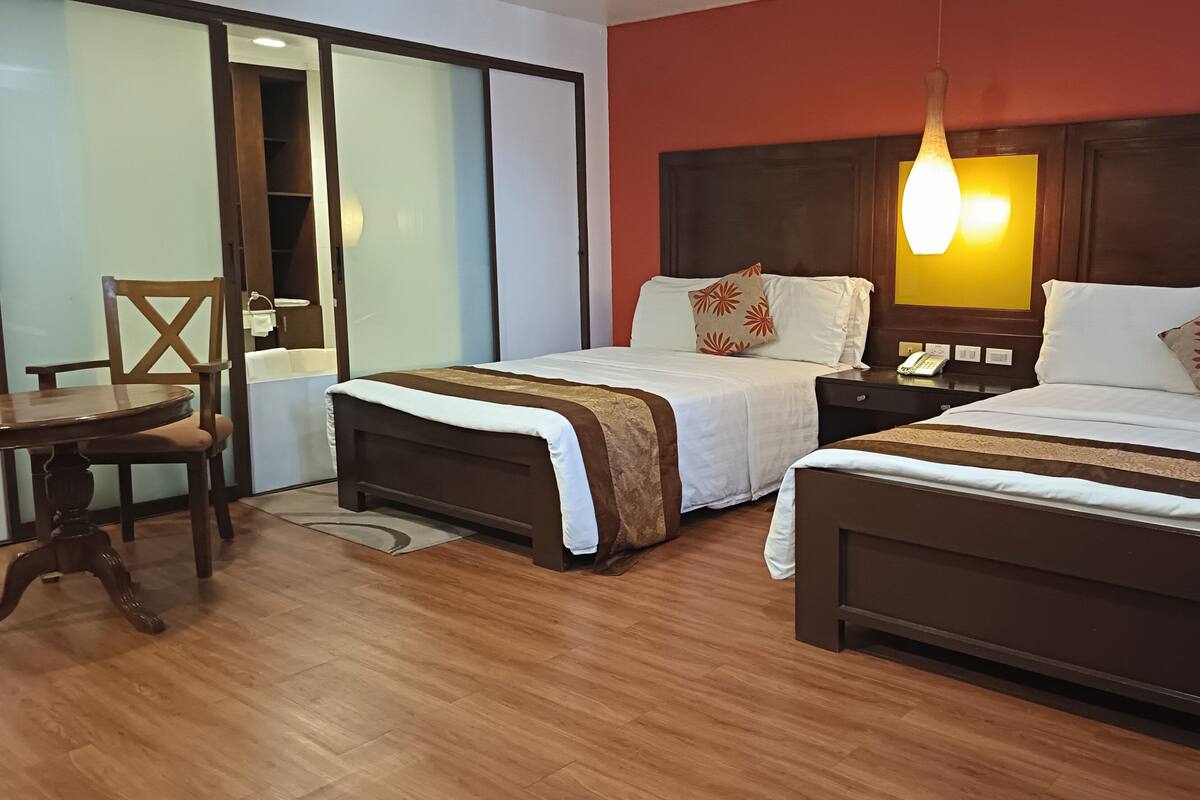 Habitación de hotel con dos camas, un escritorio de madera y una silla.