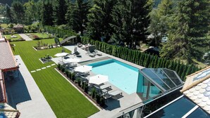 A modern outdoor pool area with lounge chairs and umbrellas, surrounded by well-maintained lawns and trees. - Renè Dolomites Boutique Hotel (San Giovanni di Fassa)