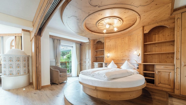 A circular bed in a wooden room with a view of greenery outside. - Renè Dolomites Boutique Hotel (San Giovanni di Fassa)