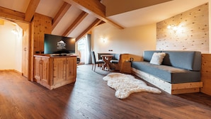 A cozy room with a wooden ceiling, a sofa, a television, and a dining area. - Renè Dolomites Boutique Hotel (San Giovanni di Fassa)