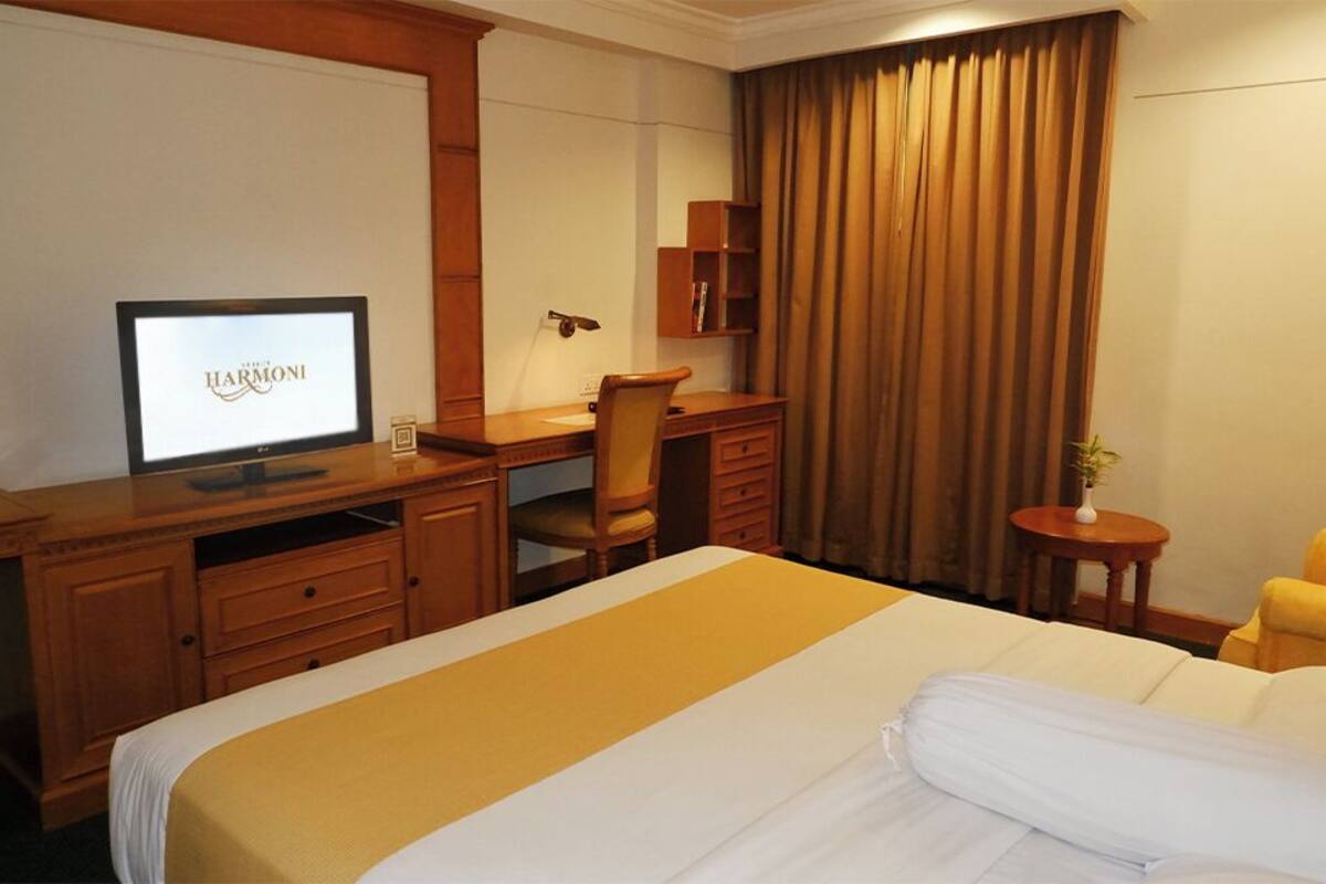 Habitación de hotel con cama, escritorio con computadora, silla, mesita y ventana con cortinas.