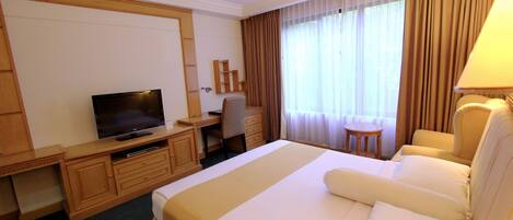 A hotel room with a large bed, a desk with a television, a chair, and a small table.