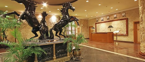 Un hall de entrada con un mostrador de recepción de mármol, dos estatuas de bronce de caballos y plantas en macetas.