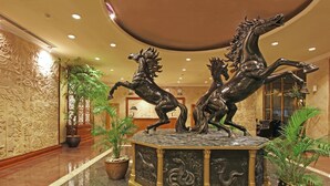 A lobby with a central decorative sculpture of horses, potted plants, and a patterned wall. - Harmoni Suites Hotel (Batam)