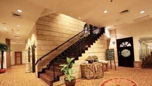 A grand staircase with a sign reading "Cafe Room A" leading to a room with a clock and a sign welcoming guests. - Harmoni Suites Hotel (Batam)