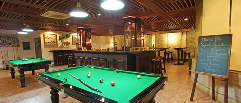 Una mesa de billar con bolas, una pizarra con texto y una zona de bar con taburetes.