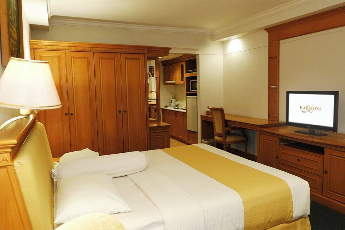 Una habitación de hotel con una cama, un escritorio con computadora, un televisor y muebles de madera.
