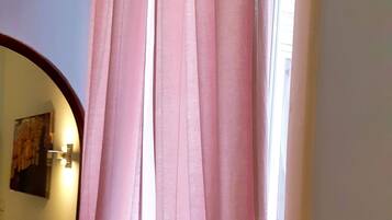 Un pasillo con una ventana cubierta por cortinas rosas, un espejo y una lámpara fijada a la pared.