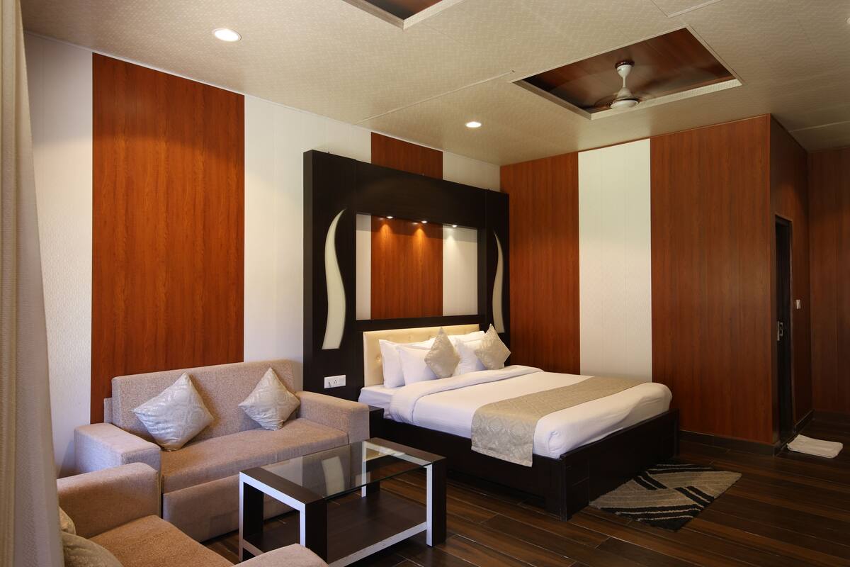 Ein modernes Hotelzimmer mit Bett, Sofa, Glastisch, Holzvertäfelung und Deckenventilator.