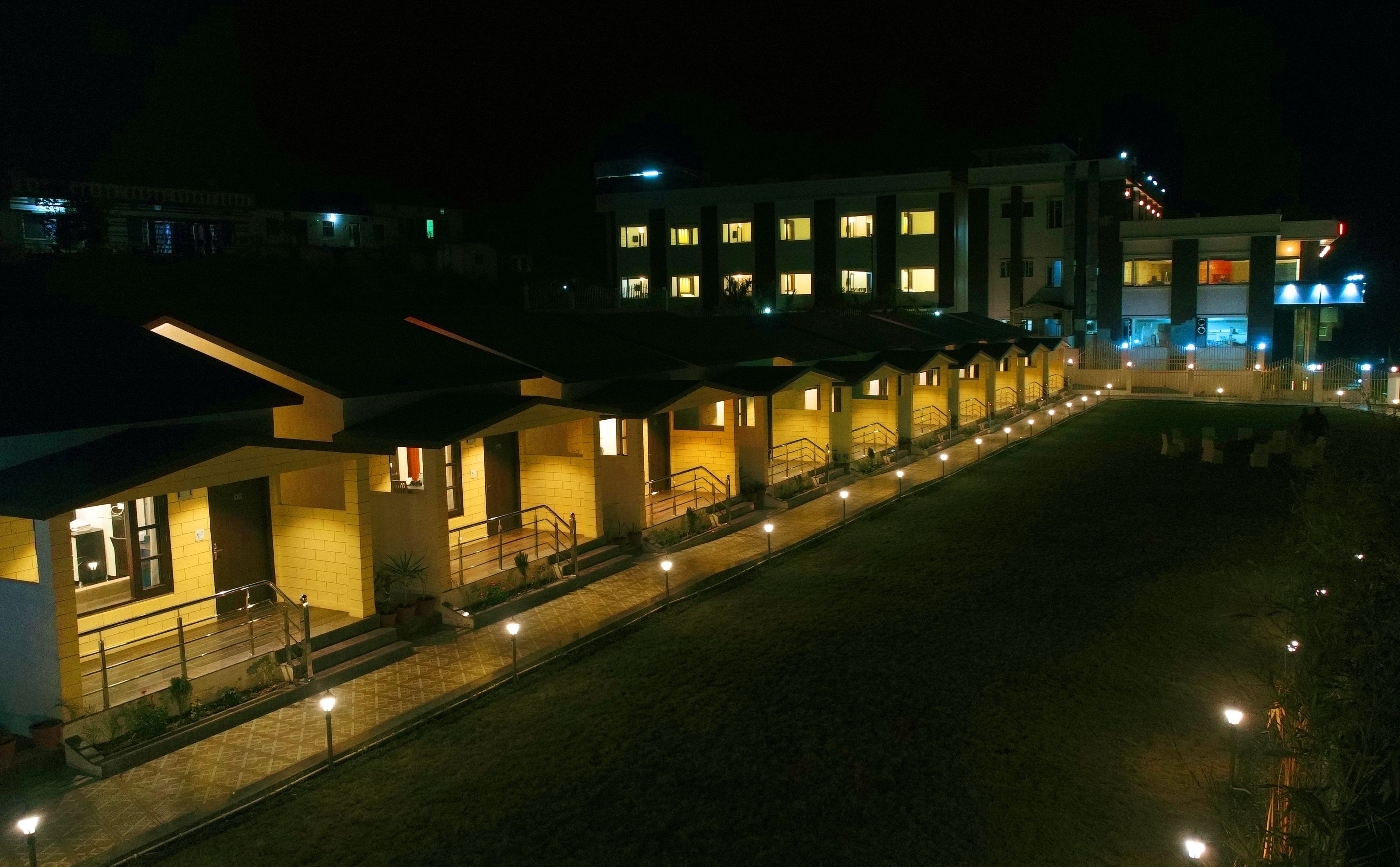A row of hotel buildings at night with illuminated windows and a paved walkway.