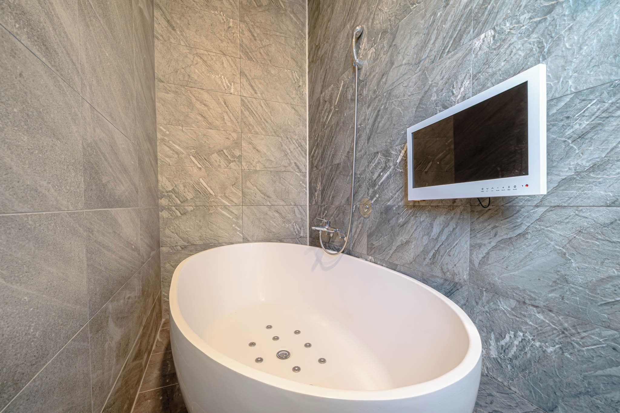 A modern bathroom with a freestanding bathtub, a handheld showerhead, and a mounted digital control panel.