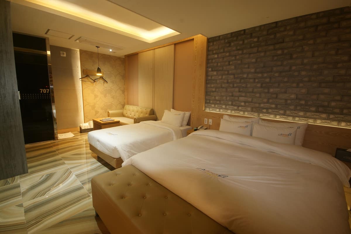 A hotel room with two beds, a sofa, a small table, and a brick-patterned wall.