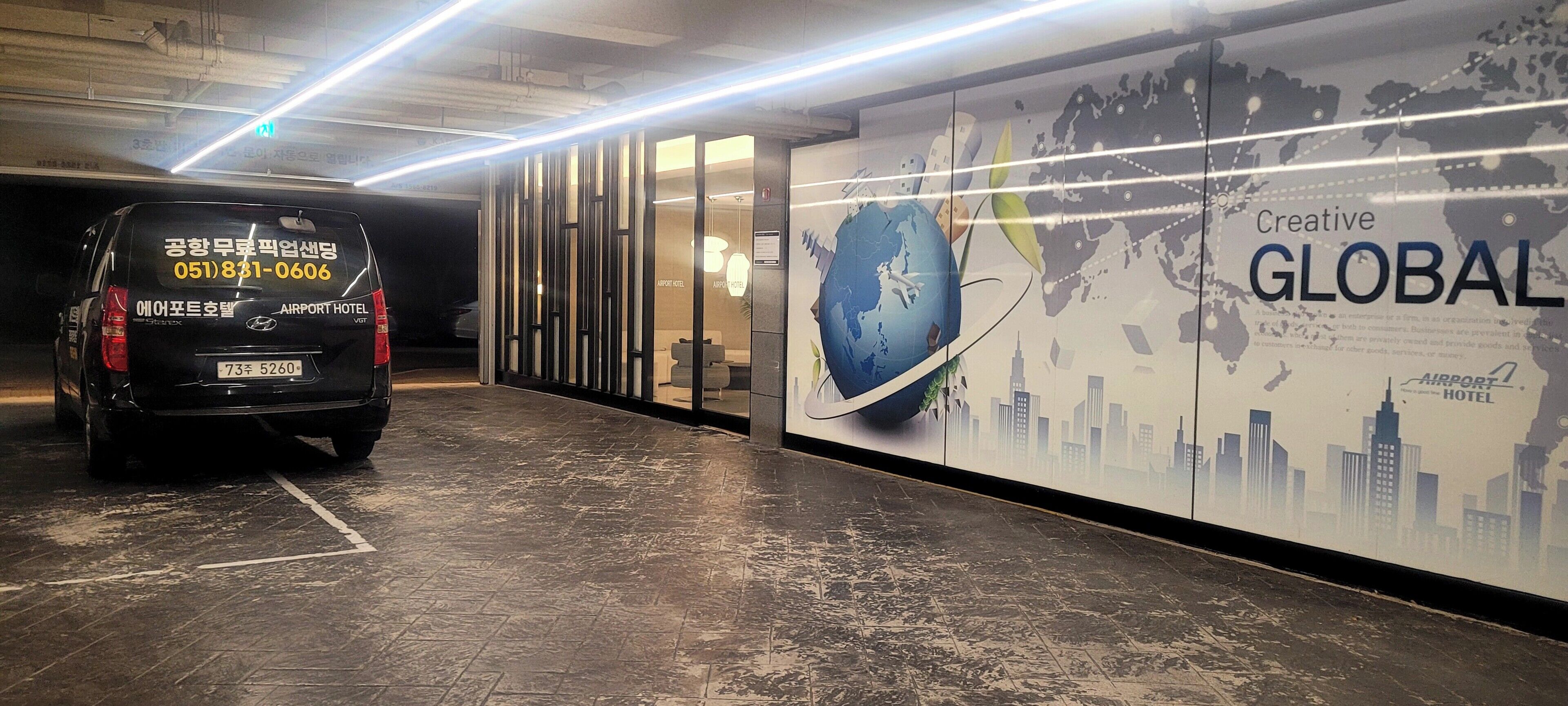 A black van parked in a hallway with a large wall advertisement for an airport hotel.