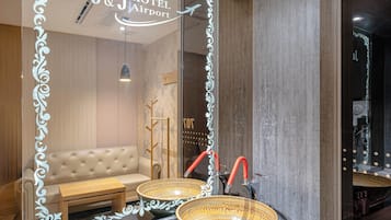 Une chambre d’hôtel avec un mur recouvert de miroirs, un canapé, une petite table et deux grands paniers en osier.