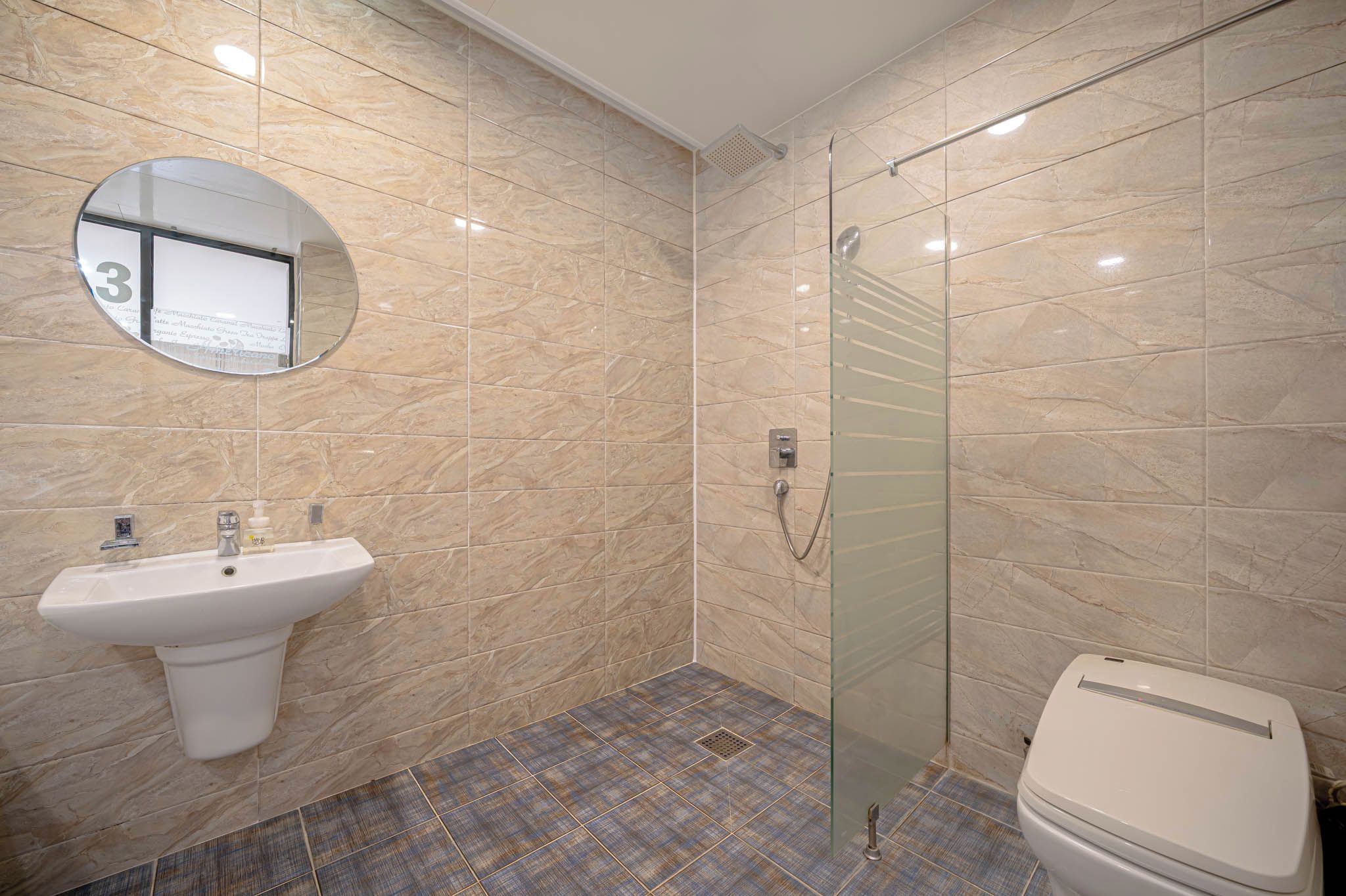 A bathroom with a marble wall, a sink, a glass shower enclosure, and a toilet.