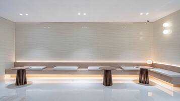 A modern, minimalist bathroom with a central bench, two round tables, and recessed lighting.