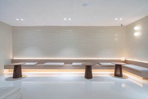 Un baño moderno y minimalista con un banco central, dos mesitas redondas e iluminación empotrada.