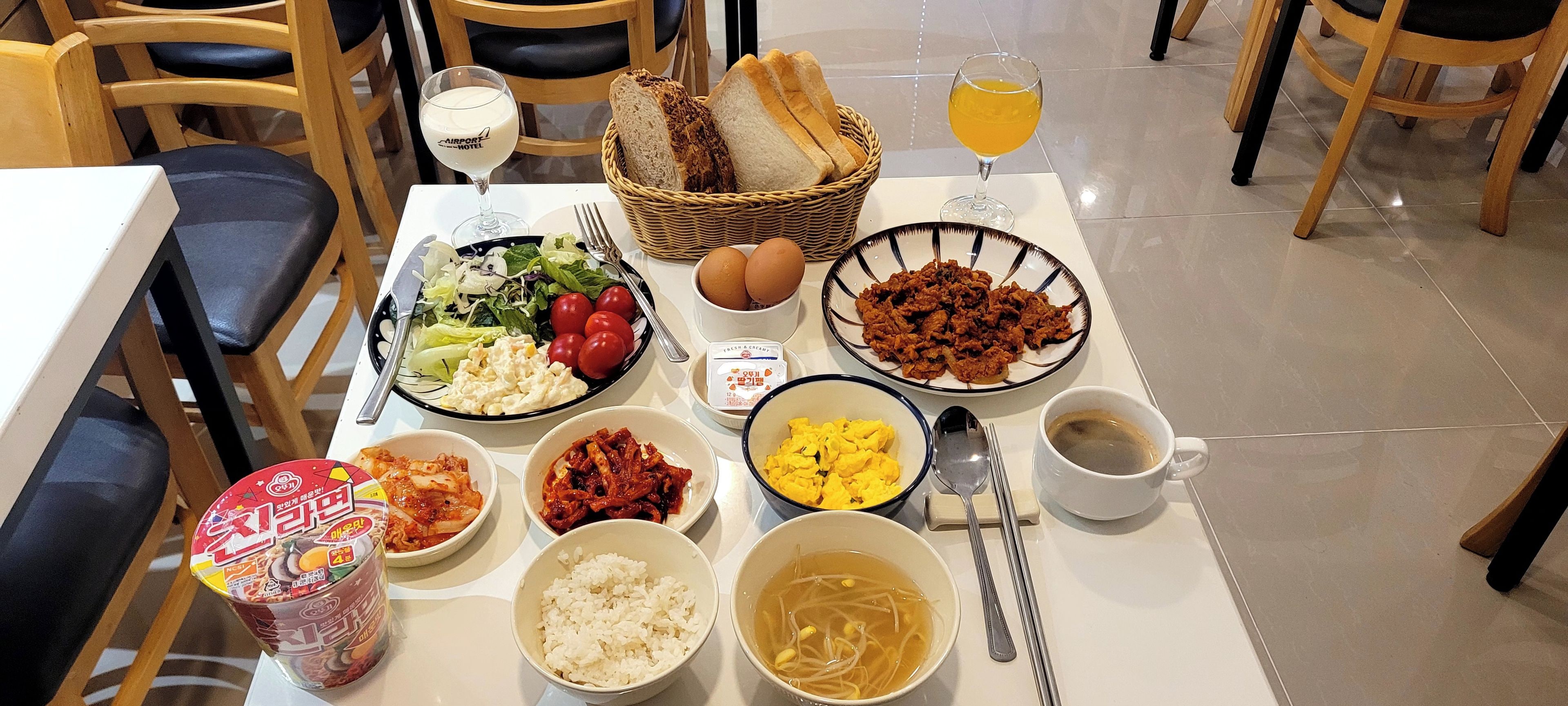 A dining table with various dishes including salad, eggs, meat, rice, and soup. There are also bread, a bottle, and a glass of juice.