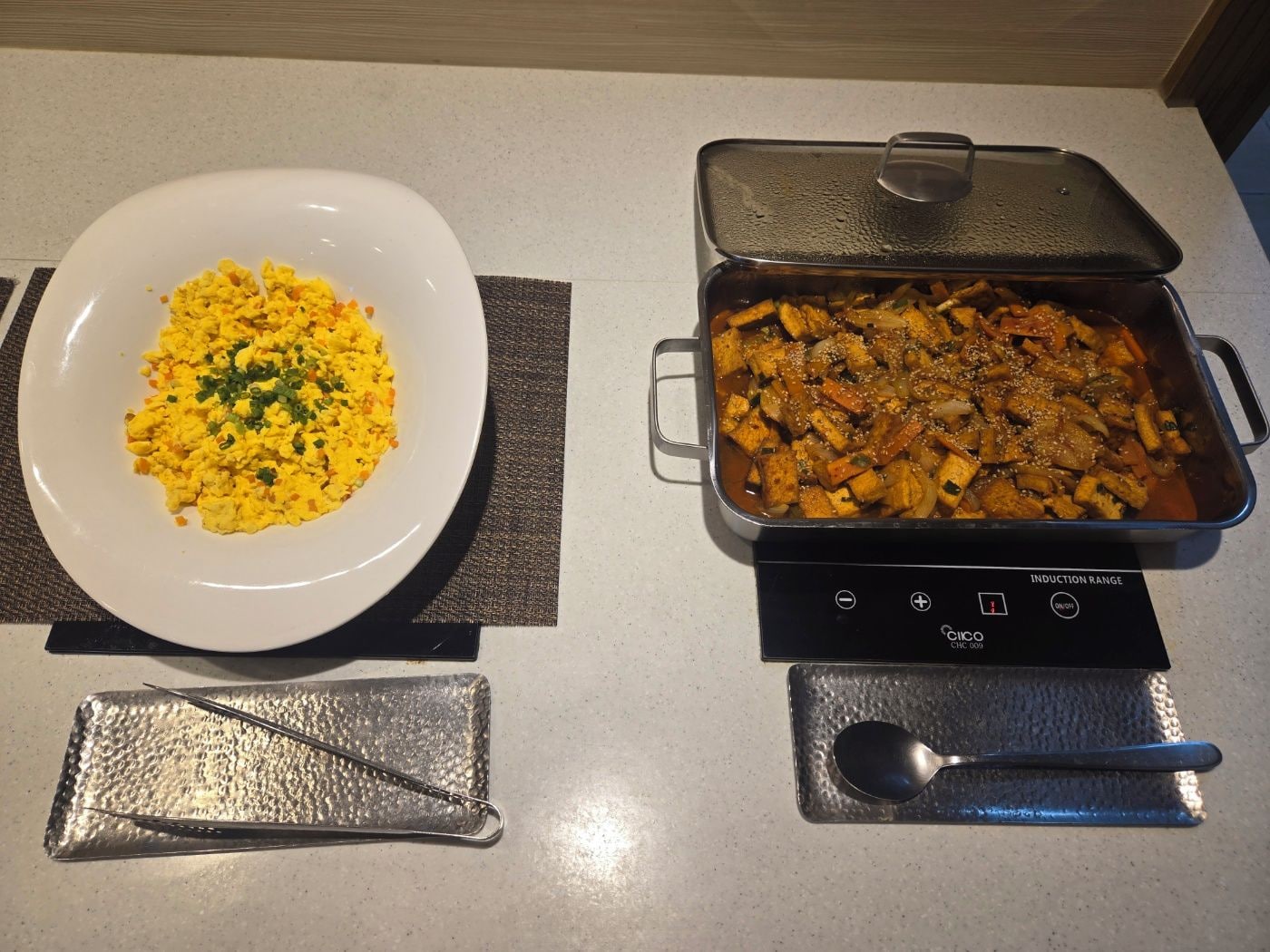 A white plate with scrambled eggs and a rectangular pan with a lid on a countertop.