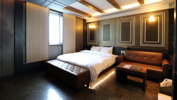 Moderni hotellihuone, jossa on suuri sänky, nahkasohva, pieni pöytä ja suuri ikkuna.