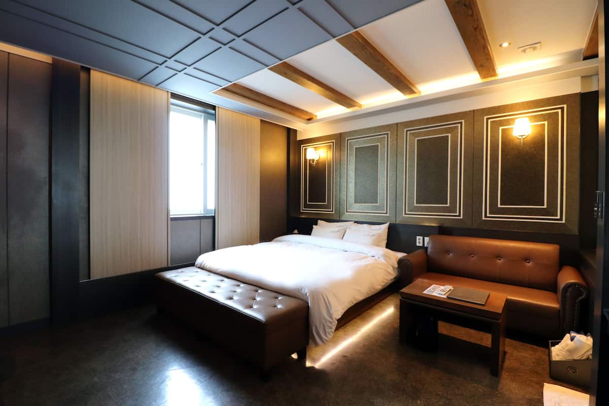 A modern hotel room with a large bed, a leather sofa, a small table, and a large window.