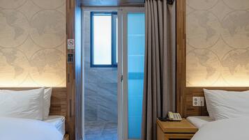 A hotel room with two beds, a sliding door to a balcony, a no-smoking sign, a phone on a bedside table, and a wall with a world map design.