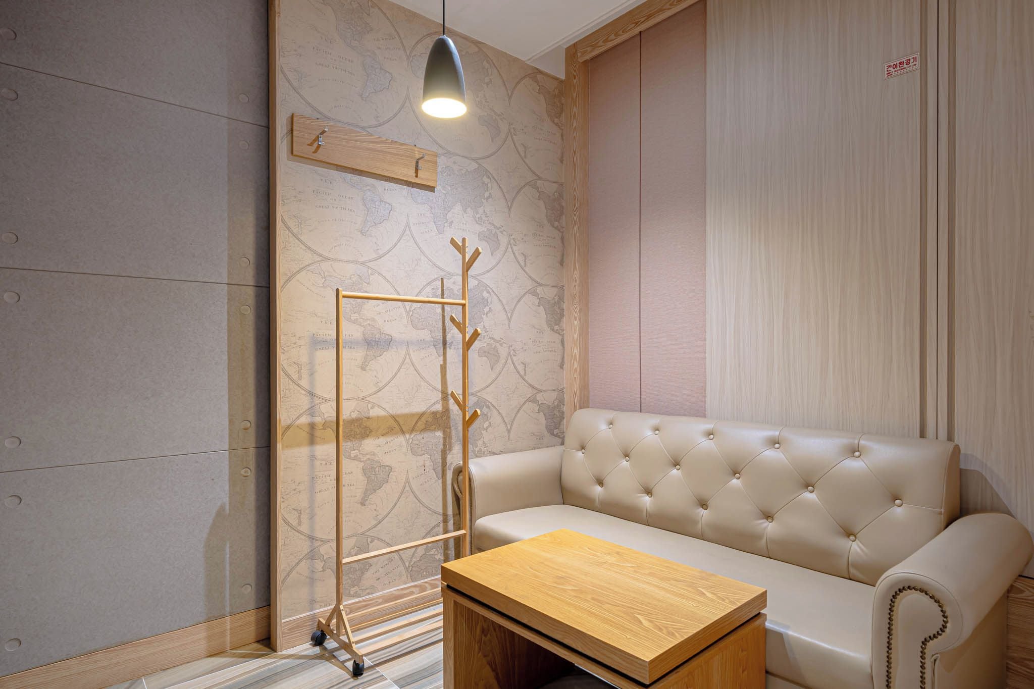 A room with a sofa, a wooden coffee table, a coat rack, and a map wallpaper.