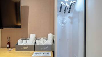 Une chambre d’hôtel avec une table en bois, deux piles de serviettes, un flacon de désodorisant et une cabine de douche en verre.