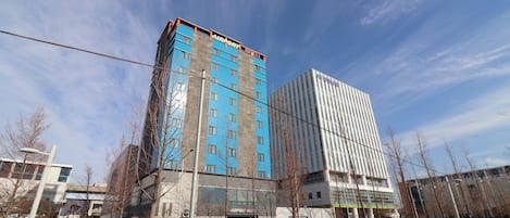 Un hotel moderno con un llamativo letrero 'AIRPORT HOTEL', que presenta una combinación de arquitectura de vidrio y hormigón, situado cerca de una carretera con coches aparcados y árboles sin hojas.