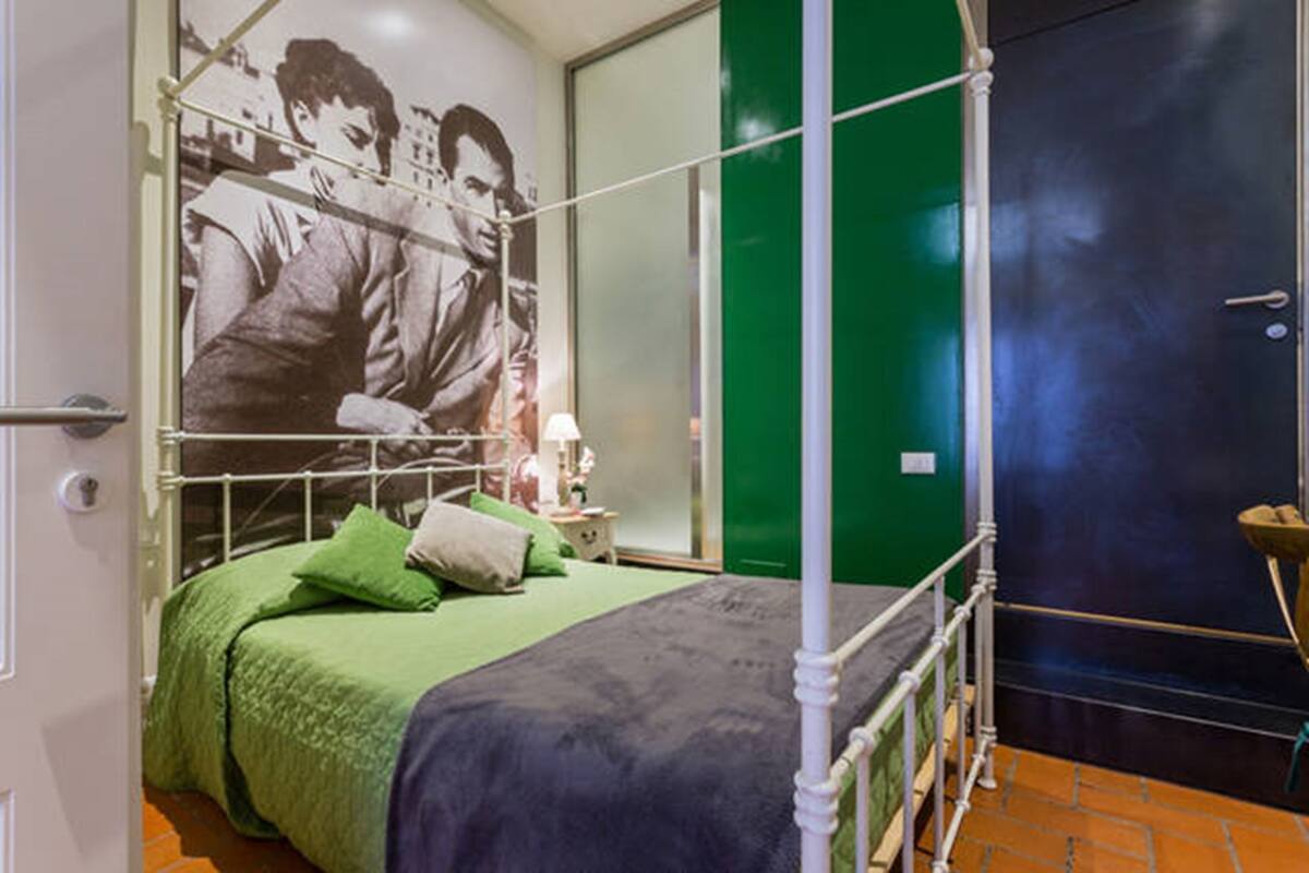 A room with a bed, green bedding, a poster on the wall, a green door, and a white metal bed frame.