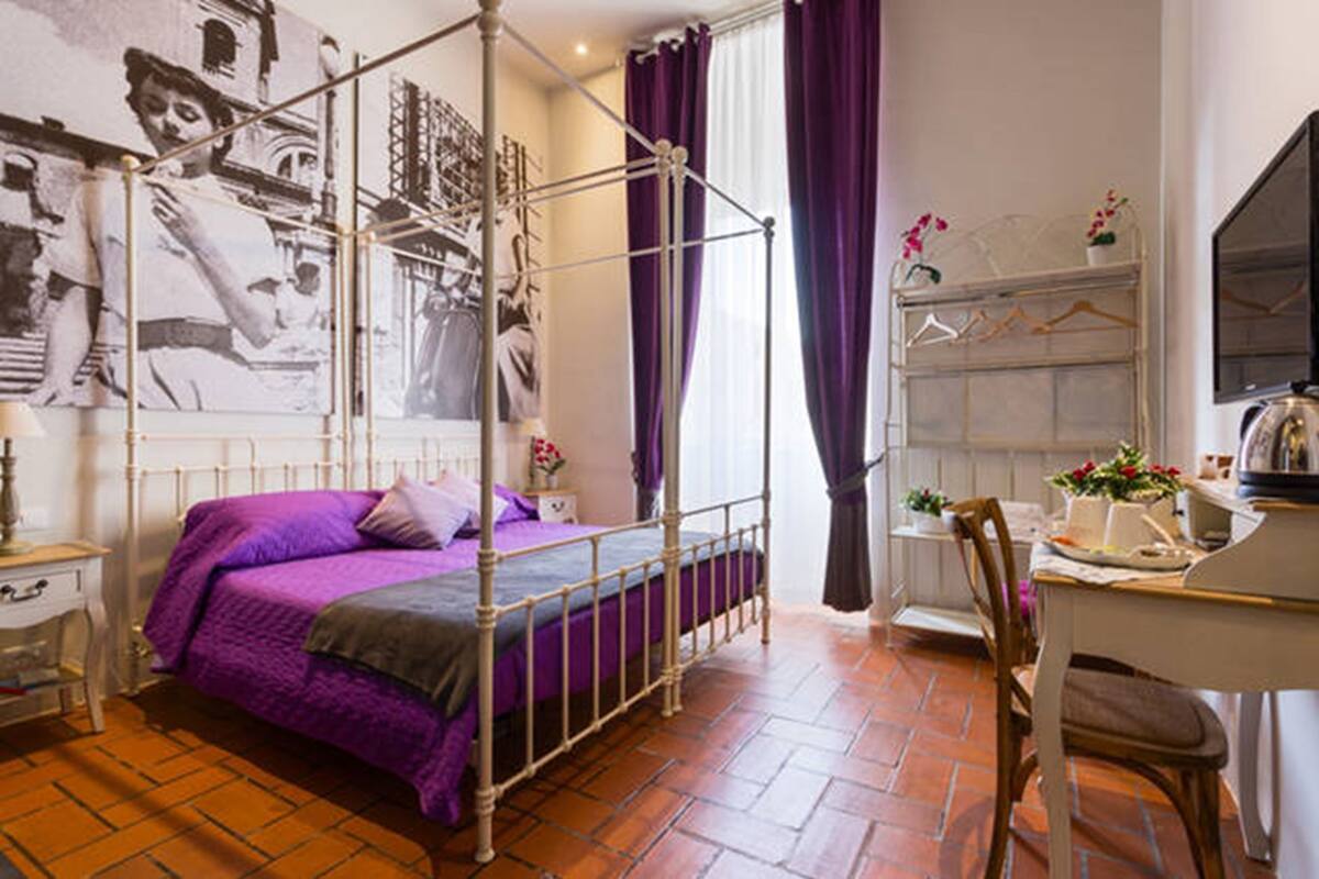 A bedroom with a four-poster bed, a desk with a chair, and a wardrobe.