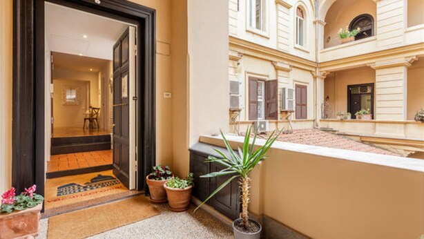 A hotel entrance with a dark wooden door, a tiled entrance mat, and potted plants. - Vacanze Romane Rooms (Rome)