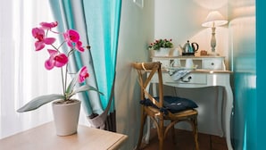 A room with a wooden chair, a desk with a lamp, a potted orchid, and a window with curtains. - Vacanze Romane Rooms (Rome)