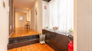 A hotel hallway with a wooden floor, a fire extinguisher, a small basket, and a window with a curtain. - Vacanze Romane Rooms (Rome)
