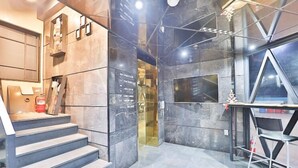 A modern hotel lobby with marble flooring, a staircase, a reception desk, and a TV screen. - 2 Heaven Hotel (Busan)