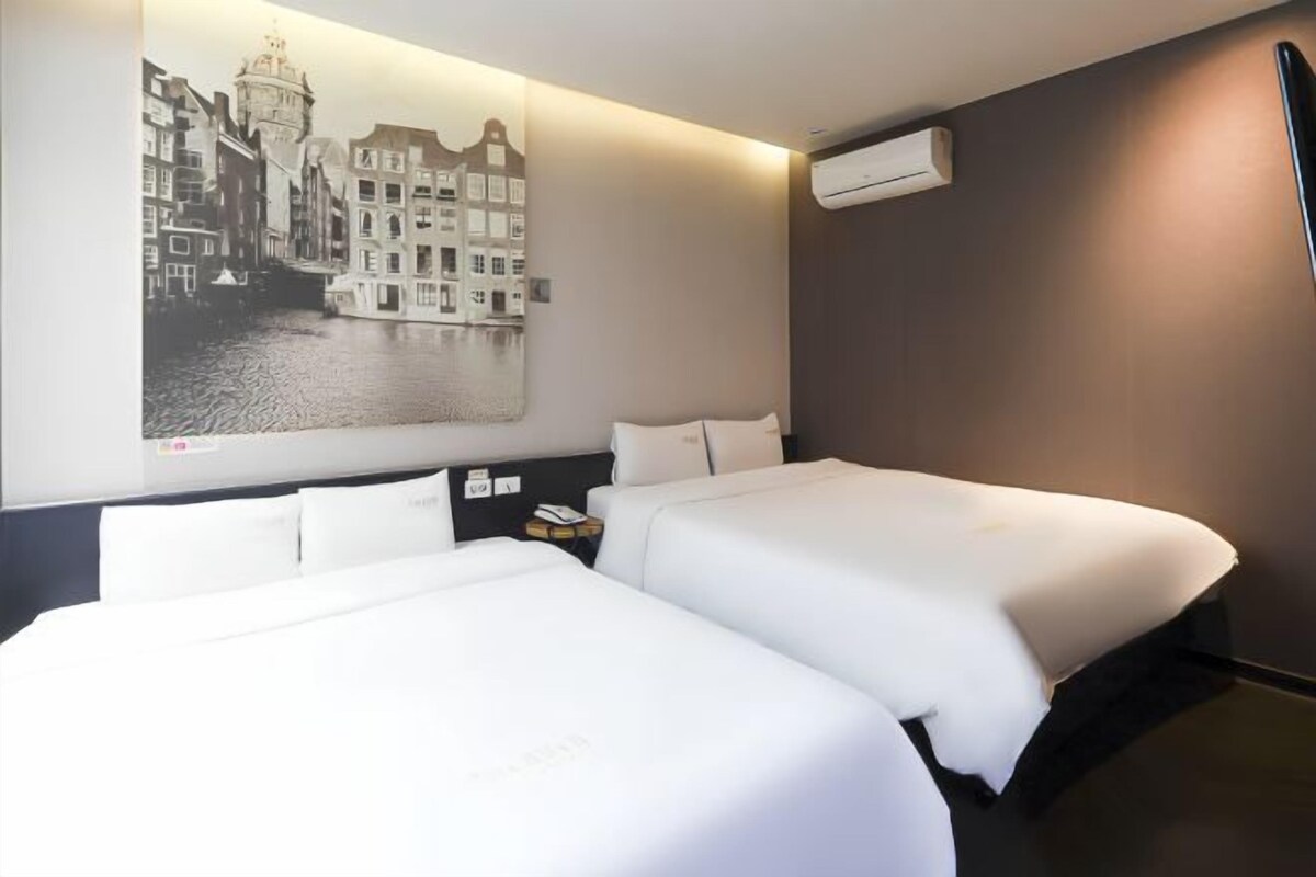 A hotel room with two beds, a large wall-mounted artwork of a cityscape, and an air conditioning unit.