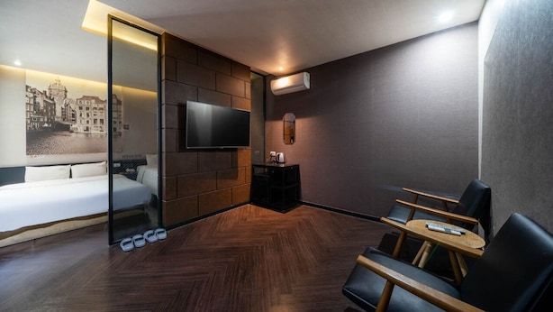 A modern hotel room with a bed, a TV, a seating area with a table, and a shoe rack. - 2 Heaven Hotel (Busan)