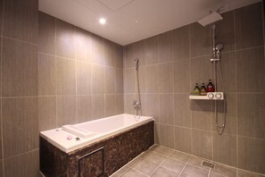 A modern bathroom with a bathtub, shower, and a shelf with toiletries. - G7 Hotel (Busan)