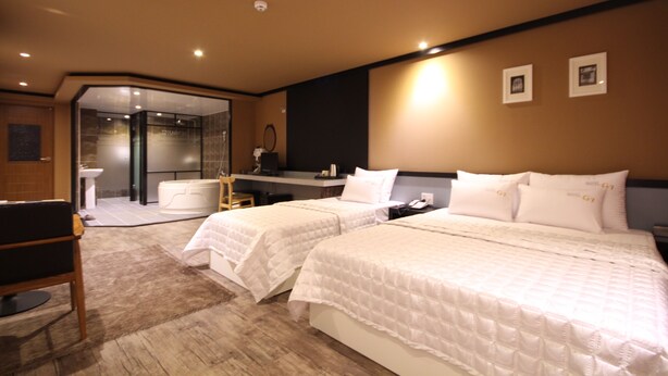A hotel room with two beds, a desk, a chair, a bathroom, and a glass-enclosed shower area. - G7 Hotel (Busan)