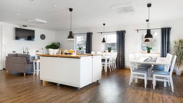 A modern kitchen with a central island, a dining area with white chairs, and a grey sofa.