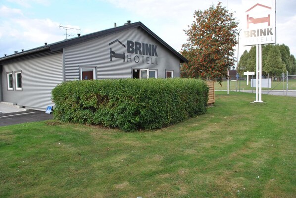 A BRINK HOTEL building with a signboard, surrounded by a well-maintained lawn and a hedge. - Brink Hotell (Eslöv)